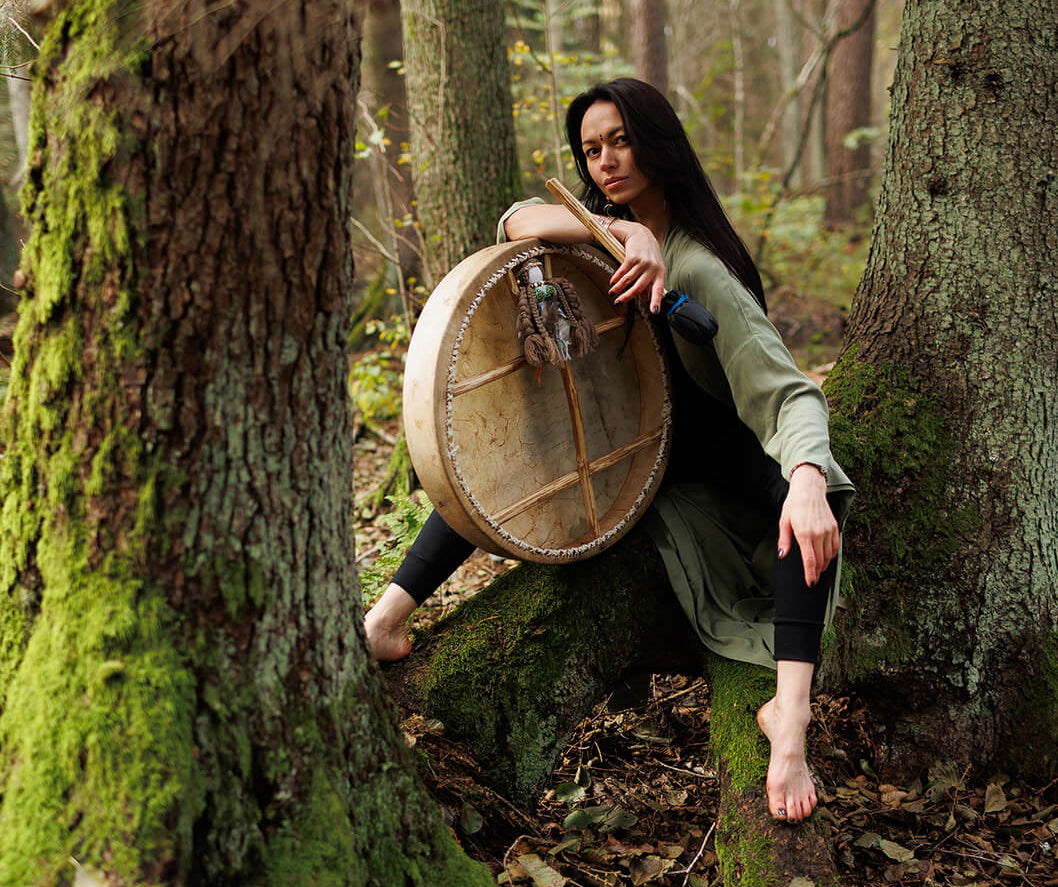Woman holding a shaman drum in a forest setting