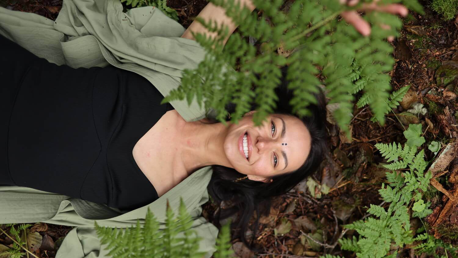 Woman lying on the forest floor surrounded by ferns