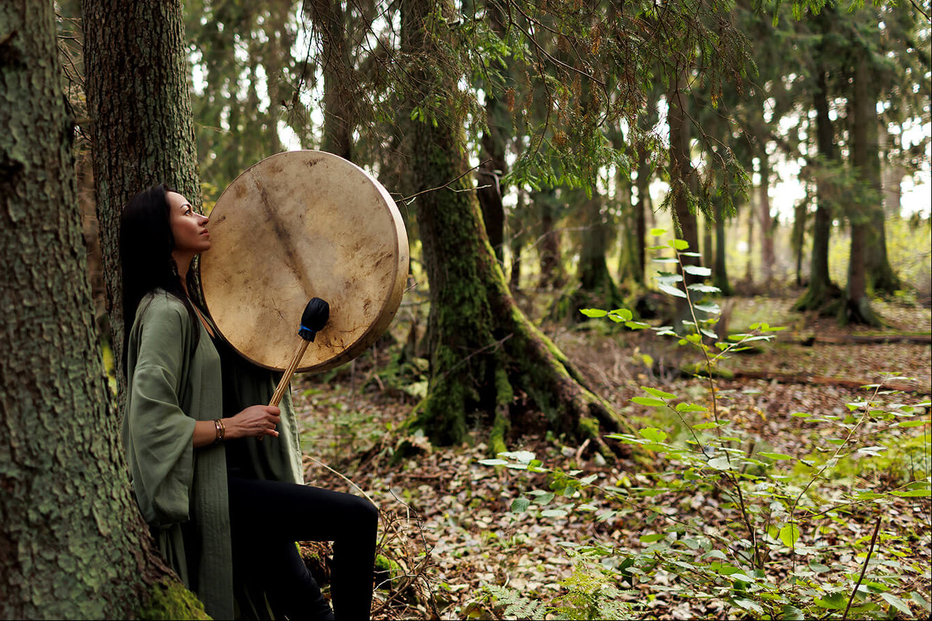 Person playing a large shaman drum in a forest setting