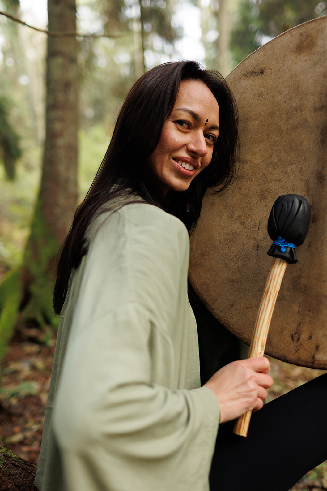 Woman holding a large shaman drum in a forest setting