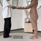 Two women standing barefoot indoors, facing each other and holding hands. One wears a loose white T-shirt and black wide-leg pants, and the other wears a beige wrap-style jumpsuit.