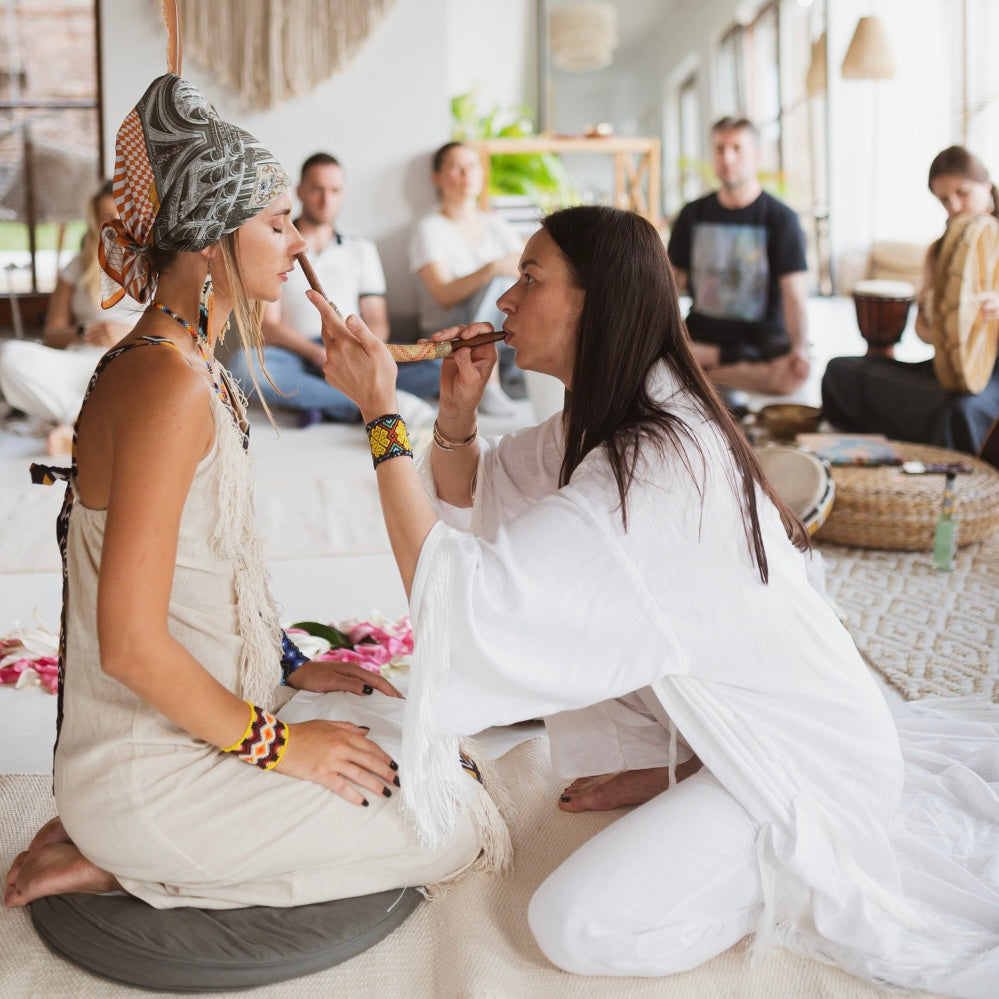 Two women sitting on the floor and making a rapeh ceremony in a room with people in the background